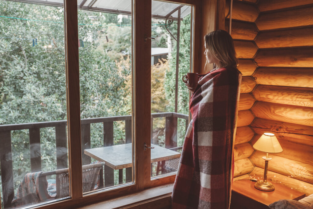 Woman Holding Coffee Looking Out a Cabin